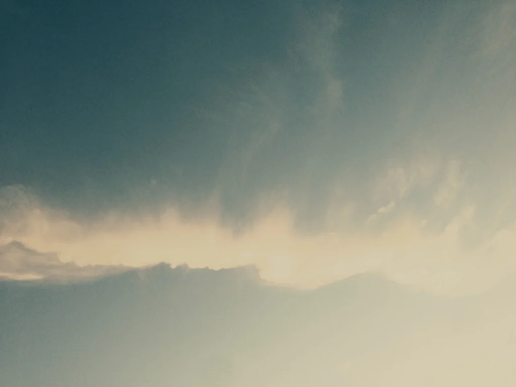A streak of white clouds stretches across a blue sky with soft sunlight illuminating the lower right corner.