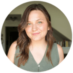 Woman with long brown hair wearing a sleeveless green top, standing indoors in front of a blurred background with bookshelves.
