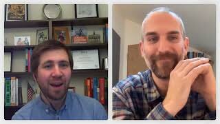 Two men participate in a video call; one is in front of a bookcase, while the other is sitting in a room with a light-colored wall and bookshelf.