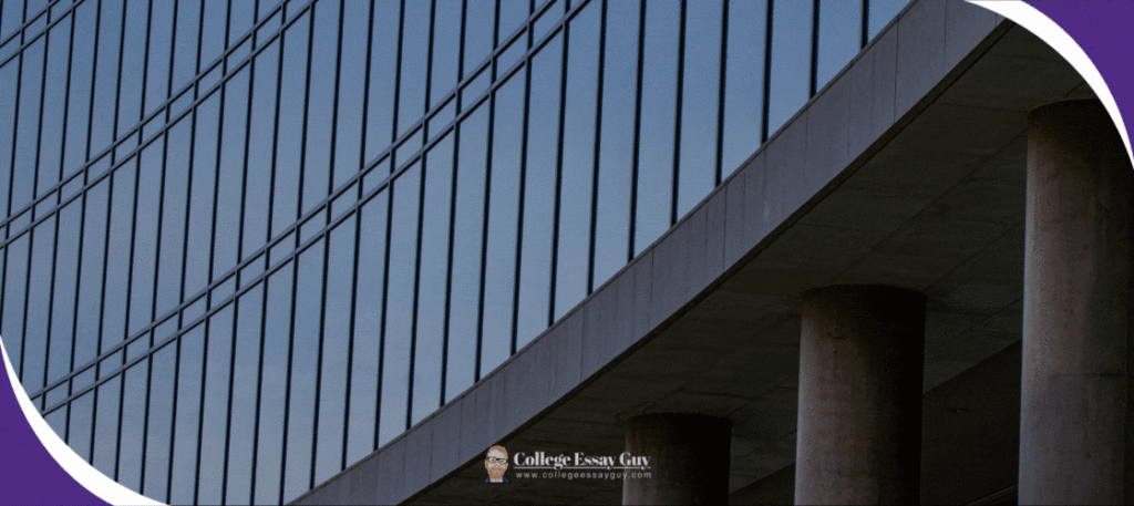 Curved concrete building with tall columns and a glass facade reflecting the sky, shown from a low angle.