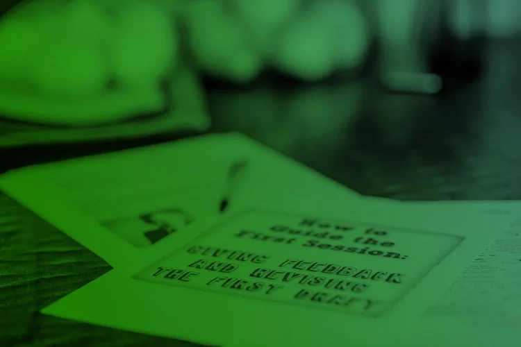 A close-up of printed papers on a table, with one sheet titled "How to Guide the First Session: Giving Feedback and Revising the First Draft." The image has a green overlay.