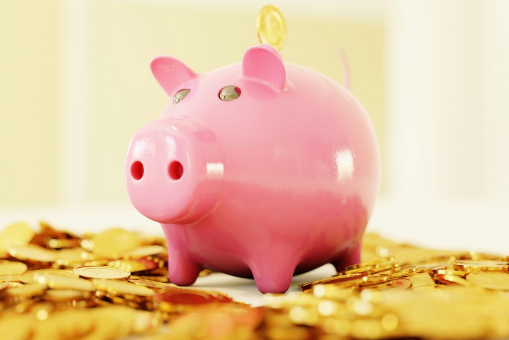 A pink piggy bank sits among scattered gold coins with a coin being inserted into the slot on its back.